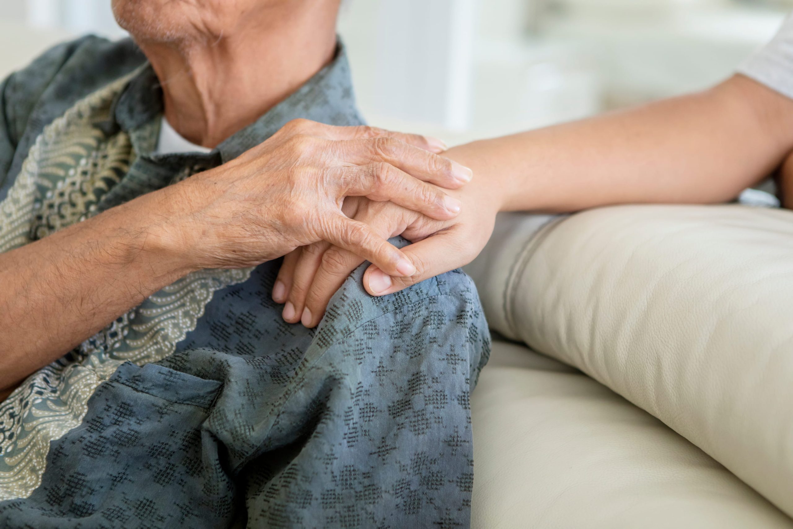Close-up of a younger person holding an elderly person's hand in comfort, showcasing the compassionate aspect of healthcare IoT.